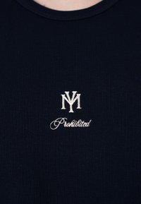 Tissu côtelé bleu marine avec logo blanc brodé combinant les lettres « N » et « M » au-dessus du mot en cursive « Prohibited » au niveau de la poitrine.