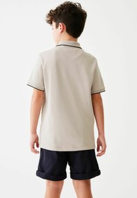 Polo beige con maniche corte e colletto, con bordi neri sugli orli delle maniche, abbinato a pantaloni corti blu navy con risvolto.