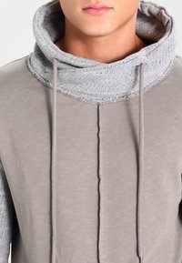 Felpa grigia con collo a cowl oversize e texture. Caratterizzata da lacci, design frontale senza cuciture e tessuto morbido.