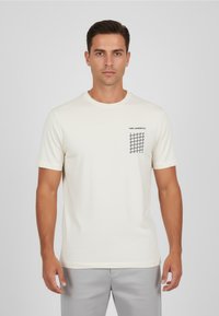 Krämfärgad t-shirt med korta ärmar tillverkad av mjukt tyg, med en svart grafik på vänster bröst och en klassisk rund halsringning.