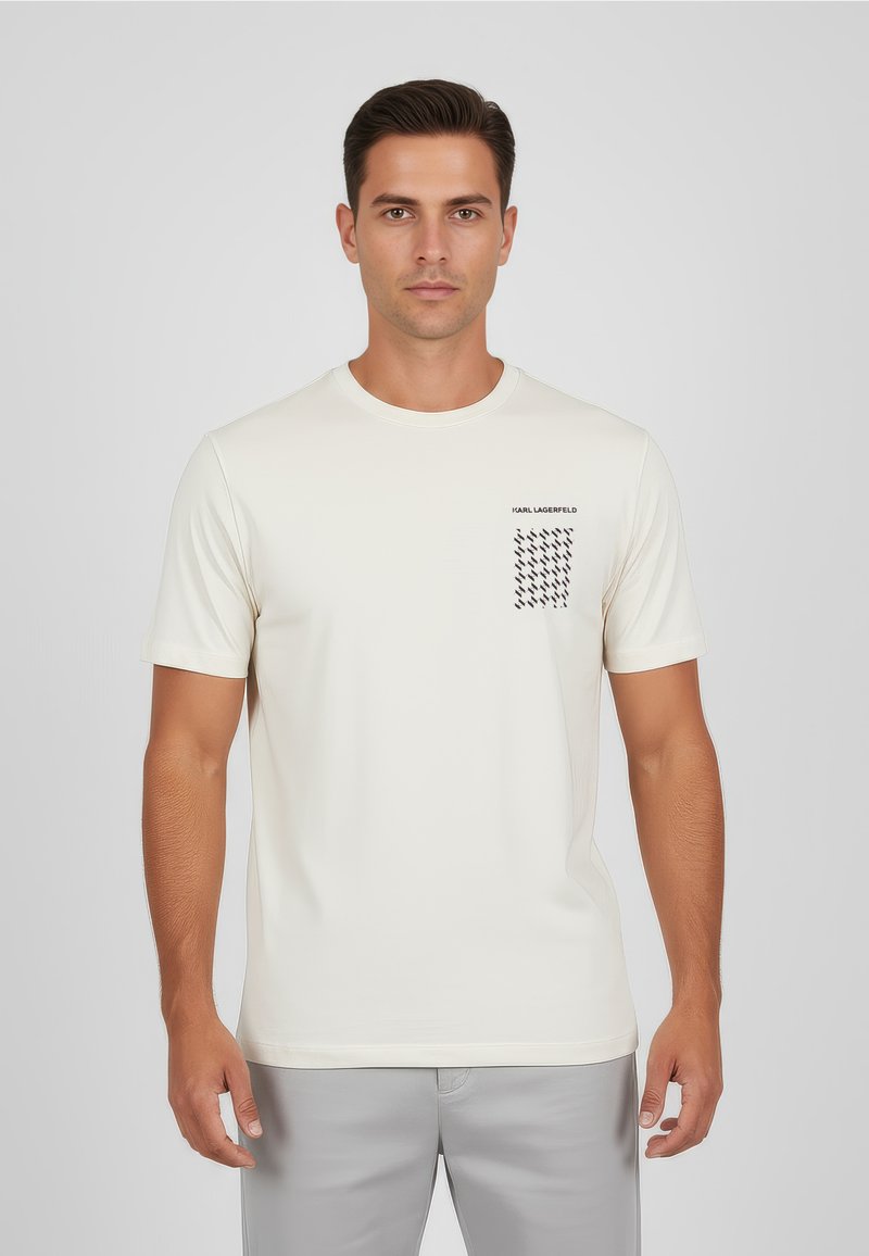 Krämfärgad t-shirt med korta ärmar tillverkad av mjukt tyg, med en svart grafik på vänster bröst och en klassisk rund halsringning.