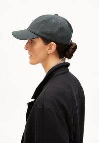 Dark green baseball cap with a curved brim, made of fabric. The design features a stitched pattern and a button on top.