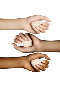 Trois mains tiennent des flacons de vernis à ongles Essie, mettant en valeur des teintes de peau variées et un vernis nude brillant et soigné. Les flacons ont une forme carrée transparente et des bouchons blancs.