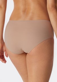 Nahtlose beige Unterwäsche mit mittelhohem Schnitt. Weicher, glatter Stoff ohne sichtbare Nähte, der einen bequemen Sitz bietet.