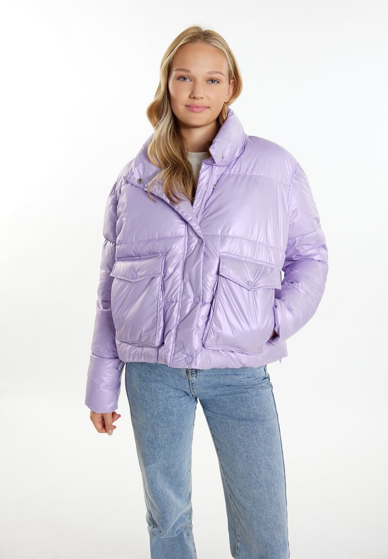 Lilla puffy jakke med høj krave, to forlommer, trykknapper og en blank, tekstureret finish. Båret med blå jeans.
