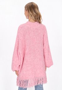 Pārmērīgi liels rozā džemperis ar rakstainu adījumu, kas piedāvā augstu apkakli un frēzētu apakšmalu. Garas, platas piedurknes un mīksts, pūkains materiāls.