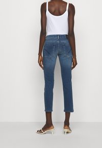 Vaqueros de mezclilla azules de corte slim, con dos bolsillos traseros y dobladillo a nivel del tobillo. Combinados con una camiseta sin mangas blanca y tacones abiertos.