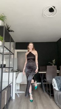 Svart satindrakt med halterneck-design, sideventil og en figurnær silhuett. Kombinert med grønne spisse hæler.
