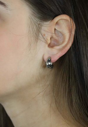 Runder, glänzender schwarzer Ohrcuff mit glatter, polierter Oberfläche, am Ohrläppchen befestigt, der ein minimalistisches Design hervorhebt.