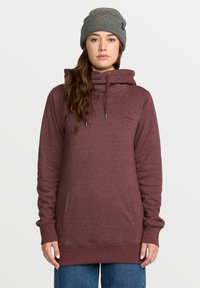 Sweat à capuche bordeaux avec un col montant, un cordon de serrage et des poches latérales. Présente des poignets et un ourlet côtelés, associé à un bonnet en tricot gris.