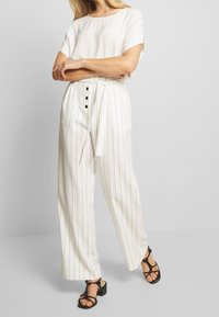 Vita randiga vida byxor med knytmidja, knappdetalj, ihop med en enkel vit t-shirt och svarta klacksandaler med blockklack.