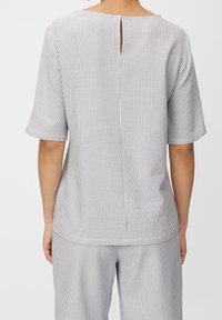 Haut rayé noir et blanc, avec manches courtes, encolure ronde et ouverture en forme de goutte d'eau dans le dos. Texture douce avec des rayures verticales.