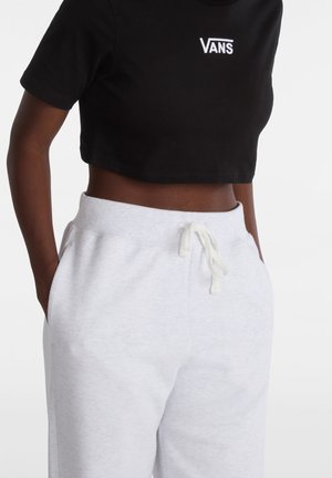 Close-up of person wearing black cropped Vans T-shirt and light gray sweatpants with drawstring, hands in pockets.