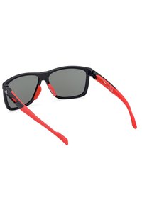 Černé sluneční brýle s šedými skly, s červenými gumovými akcenty na nožičkách a nosních podložkách. Ostře tvarovaný design s matným povrchem.
