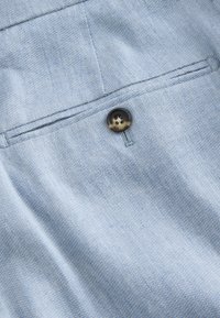 Close-up of a light blue fabric pocket with a dark round button sewn above the pocket slit on a garment.