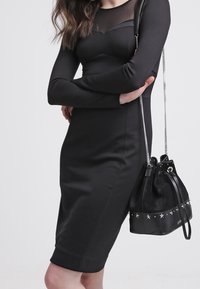 Svart långärmad klänning med genomskinlig panel vid halslinningen, figurnära siluett och knälängd på fållen. Matchad med en svart suède axelremsväska.