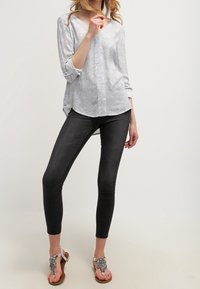 Biała bluzka z czarnym wzorem, dekolt w serek, rękawy do połowy przedramienia; w połączeniu z czarnymi obcisłymi jeansami i srebrnymi sandałami z ozdobami.