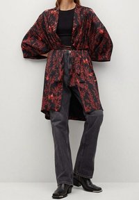 Kimono noir à motif floral rouge, manches larges, ouverture devant, ceinture à la taille. Associé à un jean gris foncé taille haute et des bottines noires.