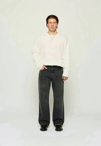 White long-sleeve shirt, relaxed fit, paired with black wide-leg jeans. Black shoes, minimal neckline, and textured fabric details visible.
