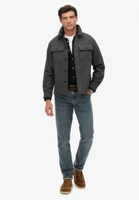 Grau melierte Wolljacke mit zwei Klapptaschen, Knopfverschluss und Hemdkragen, kombiniert mit dunklen Jeans und braunen Schnürstiefeln.