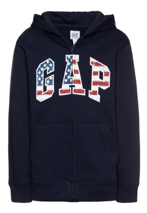 Marineblå hættejakke med lynlås lavet af blødt stof, med et stort "GAP"-logo i et mønster af røde, hvide og blå striber. To forlommer.