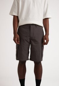 Shorts cargo gris foncé, fabriqués à partir d'un tissu léger. Comprend deux poches latérales et une fermeture à bouton. Portés avec un t-shirt beige ample.