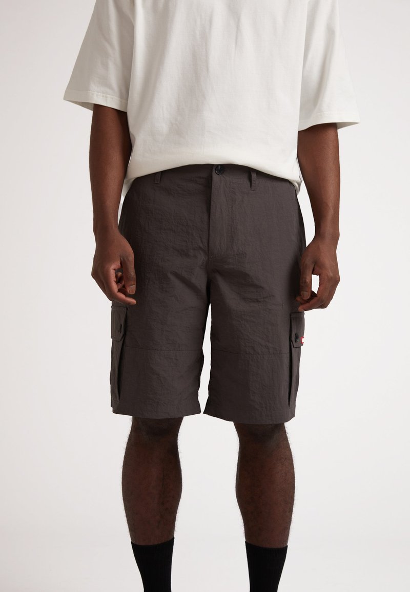 Shorts cargo gris foncé, fabriqués à partir d'un tissu léger. Comprend deux poches latérales et une fermeture à bouton. Portés avec un t-shirt beige ample.