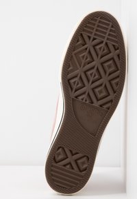 Semelle d'une chaussure Converse All Star montrant une bande de roulement en caoutchouc marron avec des motifs géométriques et le nom de la marque embossé.