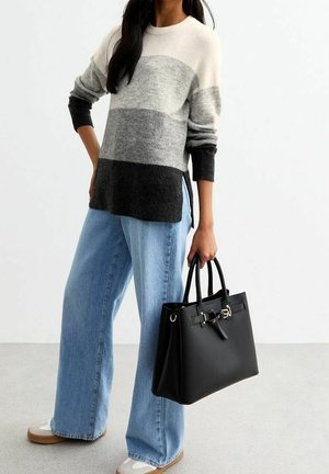 Personne portant un pull rayé gris et noir et un jean large tenant un sac à main noir structuré par les poignées.
