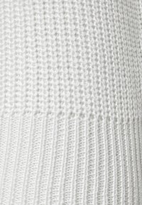 Tissu de pull en tricot blanc avec un motif texturé. Poignet côtelé en bas, créant un contraste avec la section supérieure plus lisse.