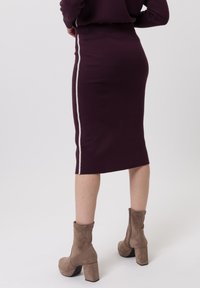 Bordeauxrode gebreide kokerrok met een witte zijstreep en een nauwsluitend silhouet, gecombineerd met beige suède enkellaarsjes met een blokhak.