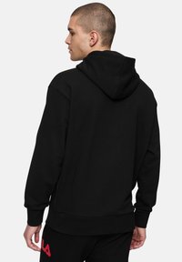 Sudadera con capucha negra de corte relajado, fabricada en un tejido suave, con puños acanalados y un discreto detalle de logo en la manga izquierda.