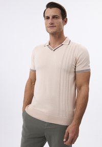 Strikket kortærmet polo i lys beige, med V-hals og kontrasterende krave samt sidelister, ribbet kant og glat tekstur.