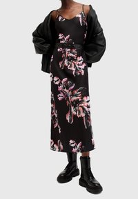 Svart blommig maxiklänning med rosa och vita bladmönster, som har tunna band och en figursydd siluett, tillsammans med en svart bomberjacka och kängor.