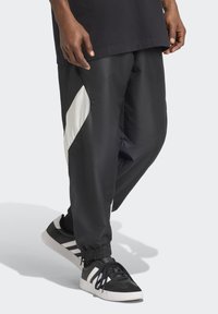 Black athletic pants with a white diagonal panel, featuring elastic cuffs and side pockets, paired with black and white sneakers.