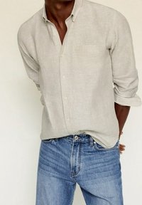 Chemise en lin gris clair avec col boutonné et une seule poche poitrine, associée à un jean en denim bleu avec un effet de décoloration verticale.