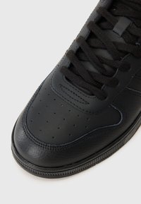 Black leather sneaker with perforated toe box, black laces, and textured side panels. Features a classic design and rubber sole.