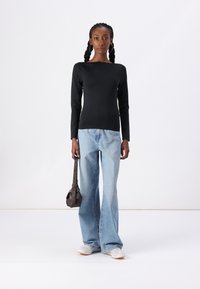 Black long-sleeve top with a square neckline, paired with light blue flared jeans. Model holds a small brown crossbody bag.