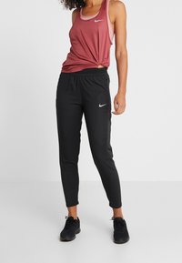 Czarne sportowe spodnie o dopasowanym kroju z perforowanymi akcentami, zestawione z różowym topem bez rękawów z wiązanym detalem.