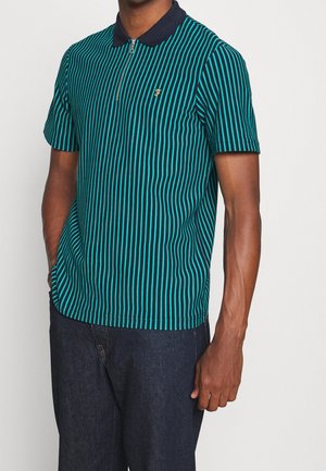 Polo à manches courtes à rayures vertes avec un col bleu marine et une fermeture à demi-zip, arborant un petit logo doré sur la poitrine gauche.