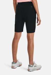 Black shorts with a tailored fit, stretchy fabric, and two back pockets. Paired with white athletic shoes featuring gray and pink accents.