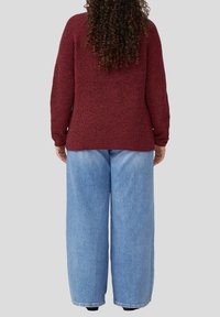 Maronenfarbener strukturierter Pullover mit langen Ärmeln und lässigem Schnitt, kombiniert mit hellblauen weit geschnittenen Jeans, die einen lässigen Lagen-Look von hinten zeigen.