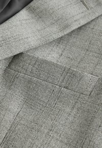 Gros plan sur un tissu gris clair avec un motif à carreaux subtil et un détail de poche fendue.