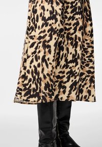 Hame leopardikuosi, joka on beige, ruskea ja musta; silkkinen rakenne, valuva muotoilu, helma polven ylle, yhdistettynä polven yli ulottuviin mustiin saappaisiin.