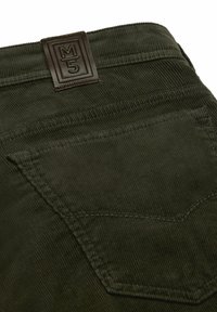 Pantalon en velours côtelé vert foncé avec une poche arrière et un patch en cuir marron étiqueté "M 5" au niveau de la taille.
