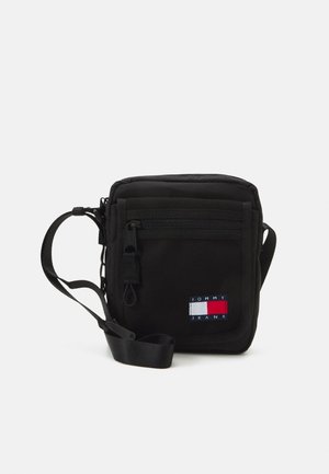 Borsa a tracolla nera realizzata in tessuto resistente, con una tasca frontale con zip, tracolla regolabile e un patch del logo Tommy Jeans in rosso, bianco e blu.
