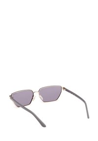 Gafas de sol estilo ojo de gato con un delicado marco de metal dorado, lentes ahumados en gris y brazos de plástico gris. Dispone de almohadillas nasales para mayor comodidad y estabilidad.