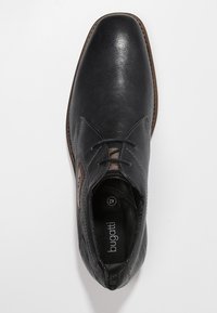 Chaussure en cuir noir à bout arrondi, présentant des détails de couture subtils, une surface texturée et un accent marron près des lacets.