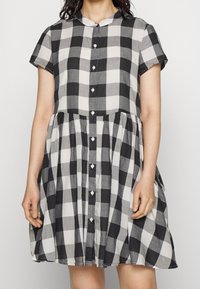 Robe à carreaux noir et blanc en tissu léger, dotée d'un col, de manches courtes et d'une fermeture à boutons, avec une jupe évasée.