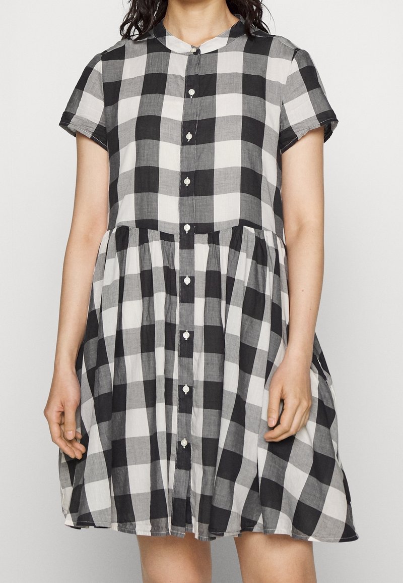 Robe à carreaux noir et blanc en tissu léger, dotée d'un col, de manches courtes et d'une fermeture à boutons, avec une jupe évasée.